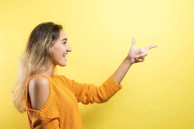 Happy young caucasian female in an orange sweater pointing fingers away