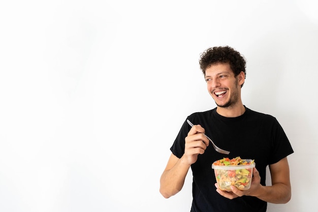Happy young caucasian man eating and holding a healthy mediterranean pasta salad