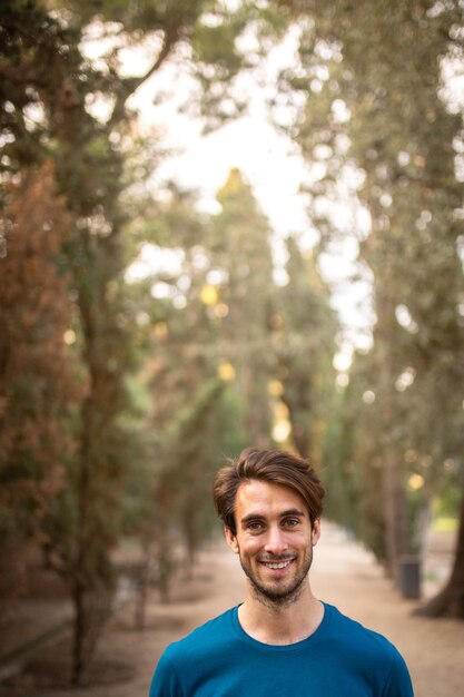 Photo happy young caucasian man standing in the forest looking at camera copy space vertical