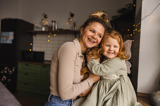 Happy young caucasian mother with redhead little daughter hugging her pet indoors Relationship concept