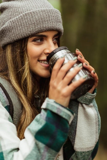 Happy young caucasian woman in jacket in forest drinks cup of tea enjoy travel vacation and hot