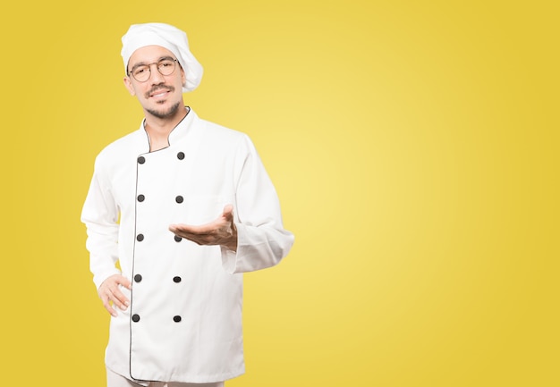 Felice giovane chef facendo un gesto di benvenuto con la mano