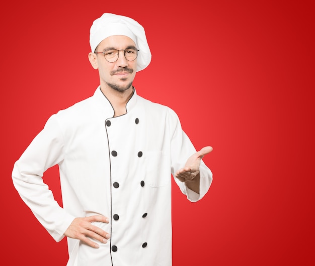 Happy young chef doing a gesture of welcome with his hand