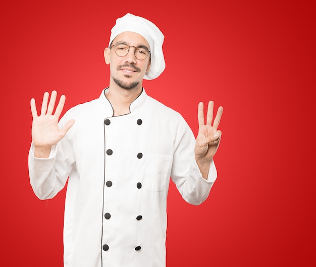 Happy young chef doing a number eight gesture with his hands