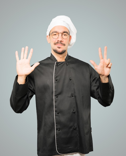 Happy young chef doing a number eight gesture with his hands