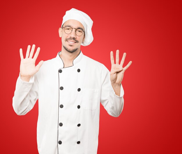 Happy young chef doing a number nine gesture with his hands