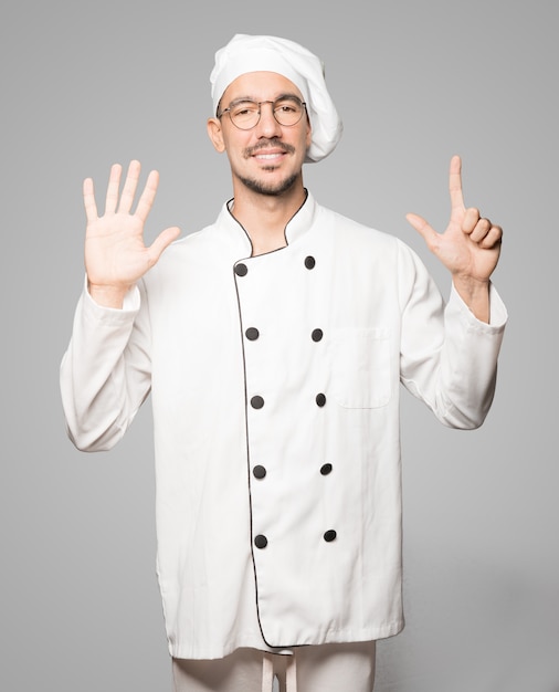 Happy young chef doing a number seven gesture with his hands