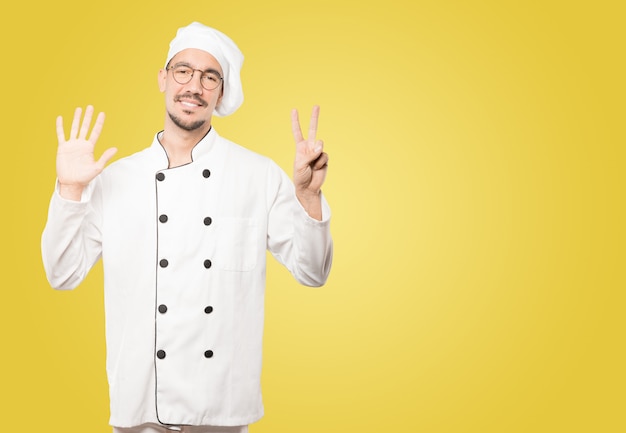Счастливый молодой шеф-повар делает номер семь жестом своими руками