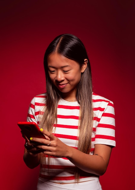 Happy young chinese woman smiling while sending message on red background