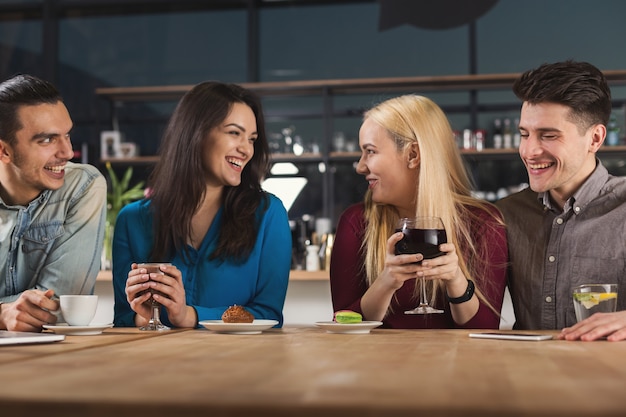 現代のコーヒーショップ、コピースペースに座ってコーヒーを飲みながら話している友人の幸せな若い会社。