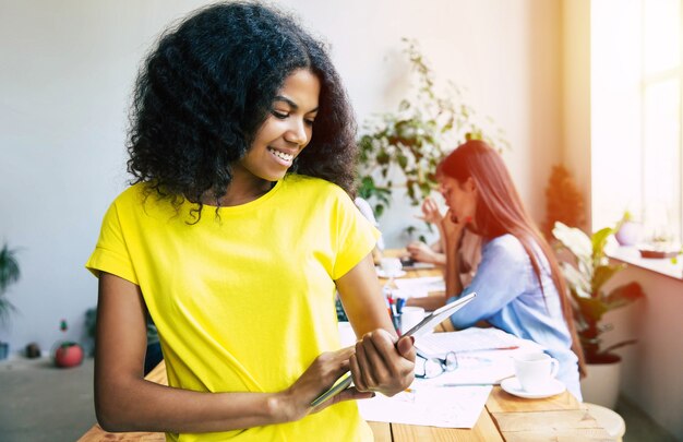 Happy young confident beautiful african business woman in smart casual wear is posing on modern business team background. Co-workers. Start up team. Students together