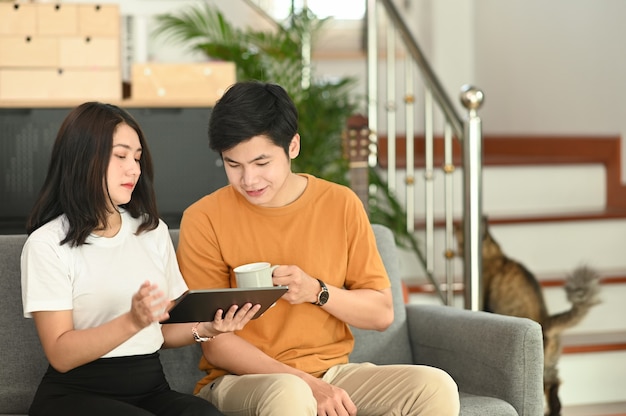 幸せな若いカップルはソファに座って自宅でデジタルタブレットを使用しています