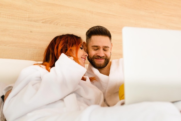 Happy young couple in bathrobes lie in bed