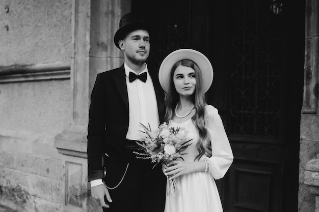 Happy young couple brides in hats young girl in a white wedding\
dress and hat with a bouquet of flowers brides in the castle bride\
and groom