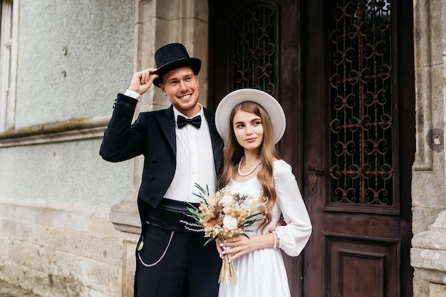 Happy young couple brides in hats young girl in a white wedding\
dress and hat with a bouquet of flowers brides in the castle bride\
and groom