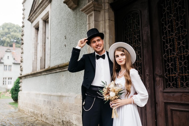 Happy young couple brides in hats young girl in a white wedding\
dress and hat with a bouquet of flowers brides in the castle bride\
and groom