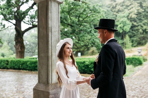 Happy young couple brides in hats young girl in a white wedding\
dress and hat with a bouquet of flowers brides in the castle bride\
and groom