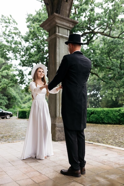 Happy young couple brides in hats young girl in a white wedding\
dress and hat with a bouquet of flowers brides in the castle bride\
and groom