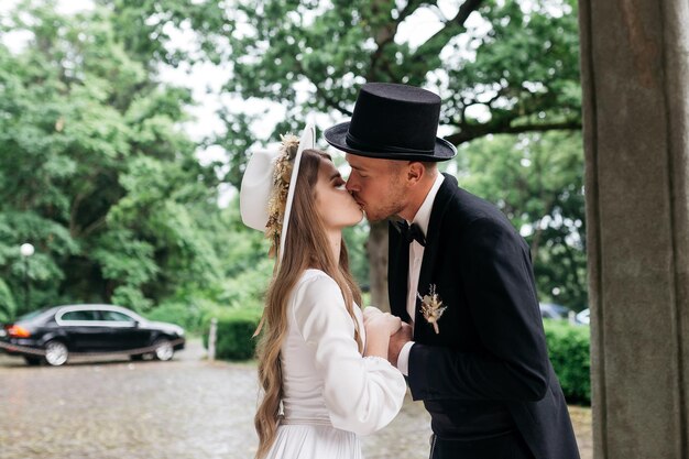 Photo happy young couple brides in hats young girl in a white wedding dress and hat with a bouquet of flowers brides in the castle bride and groom