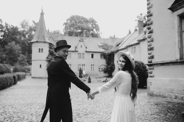 Happy young couple Brides in hats Young girl in a white wedding dress and hat with a bouquet of flowers Brides in the castle Bride and groom