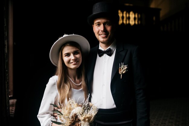 Happy young couple brides in hats young girl in a white wedding\
dress and hat with a bouquet of flowers brides in the castle bride\
and groom