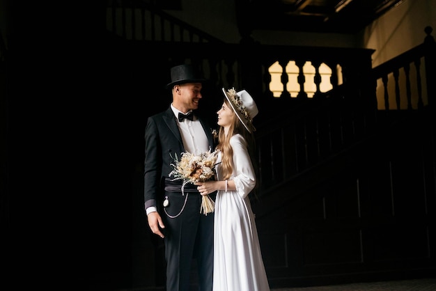 Happy young couple Brides in hats Young girl in a white wedding dress and hat with a bouquet of flowers Brides in the castle Bride and groom