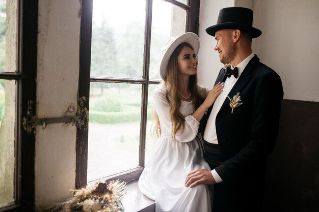 Happy young couple brides in hats young girl in a white wedding\
dress and hat with a bouquet of flowers brides in the castle bride\
and groom