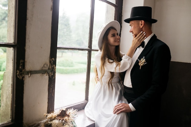 Happy young couple brides in hats young girl in a white wedding\
dress and hat with a bouquet of flowers brides in the castle bride\
and groom