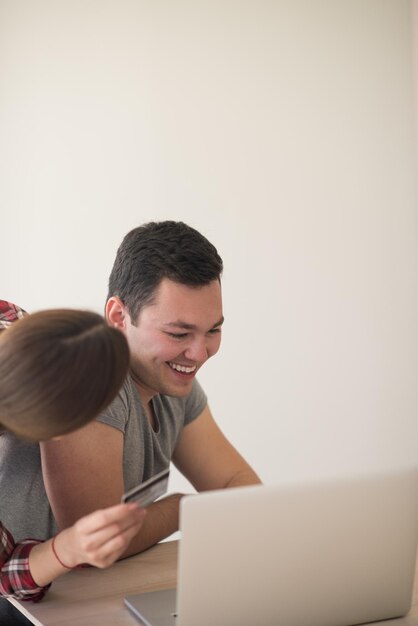 happy young couple buying online using laptop a computer and a credit card in their luxury home villa