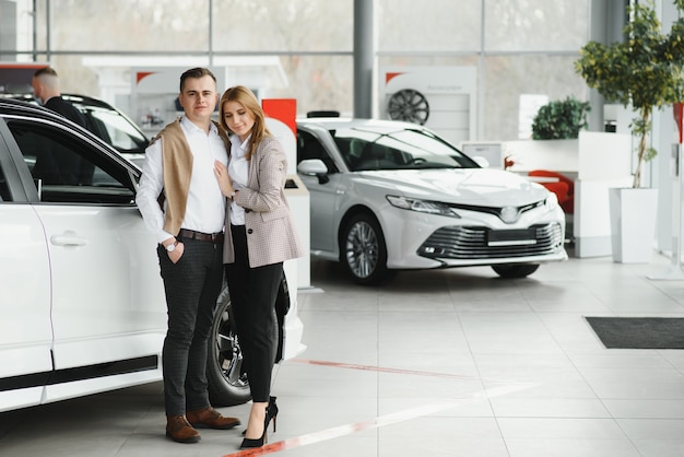 Happy young couple chooses and buying a new car for the family in the dealership.