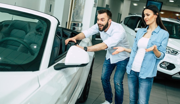 幸せな若いカップルは、ディーラーで家族のために新しい車を選んで購入します