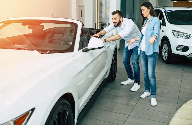 Happy young couple chooses and buying a new car for the family in the dealership