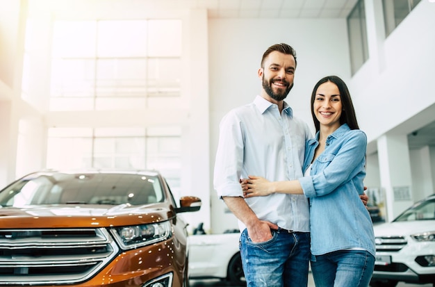 Happy young couple chooses and buying a new car for the family in the dealership