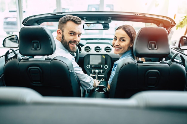 Happy young couple chooses and buying a new car for the family in the dealership