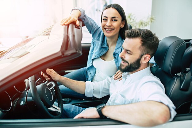 Happy young couple chooses and buying a new car for the family in the dealership