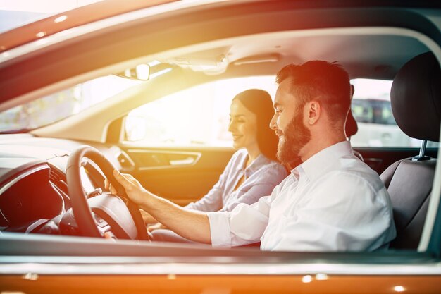 Happy young couple chooses and buying a new car for the family in the dealership