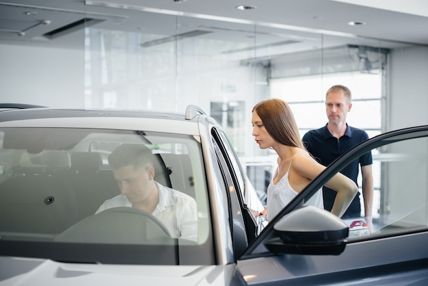 A happy young couple chooses and buys a new car at a car dealership. Buying a new car.