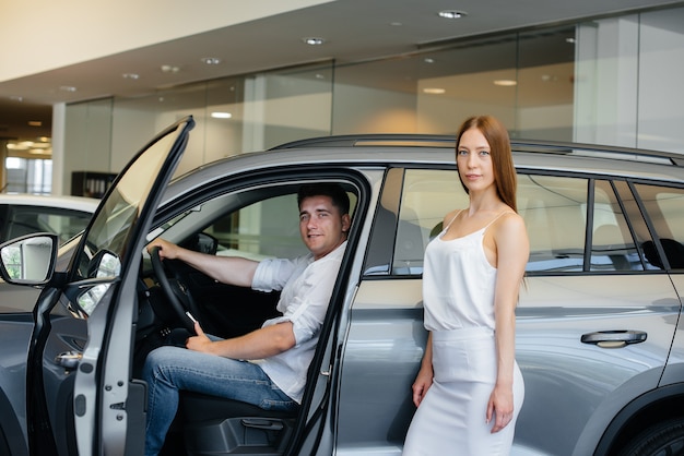 Happy young couple chooses and buys a new car at a car dealership