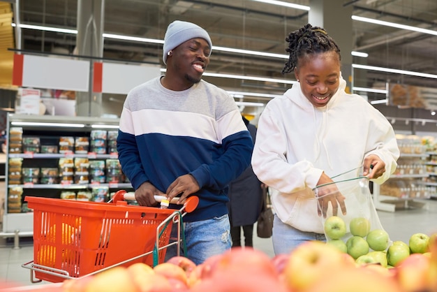 Happy young couple choosing fresh fruits while standing by display