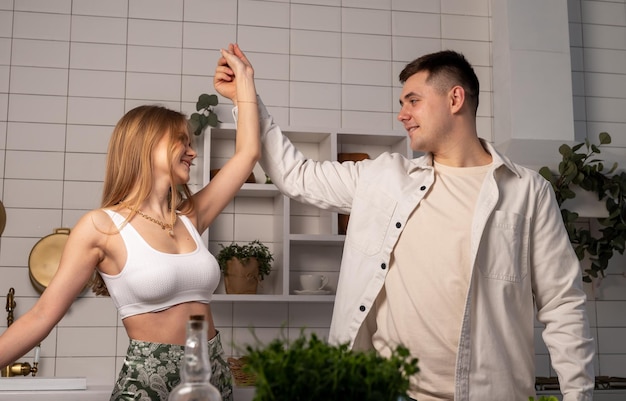 Happy young couple dancing in modern kitchen while cooking smiling wife and husband having fun and m