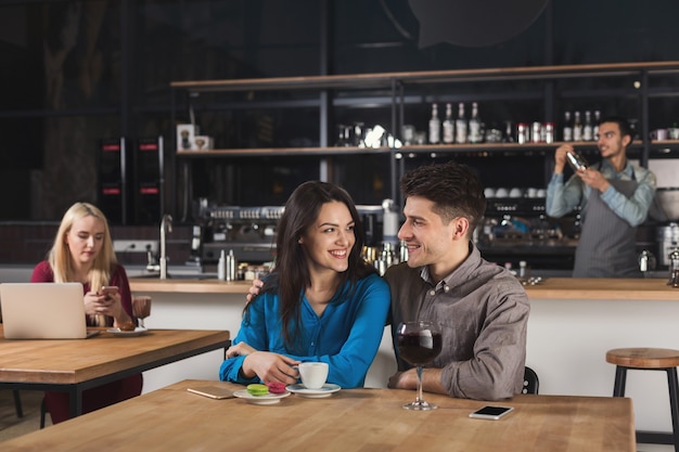 Happy young couple drinking coffee, talking and smiling while sitting at modern bar interior, copy space.