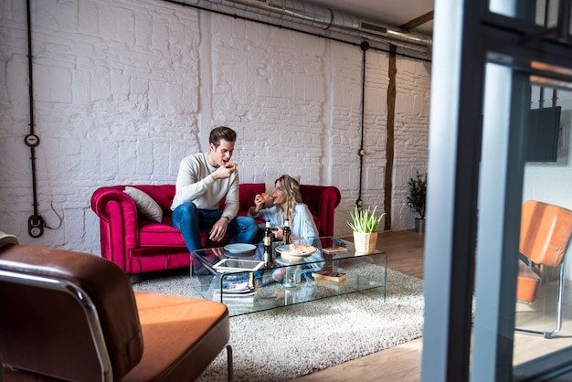 Photo happy young couple eating a pizza on the couch