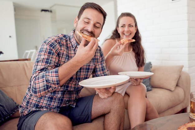 リビング ルームでピザを食べて幸せな若いカップル