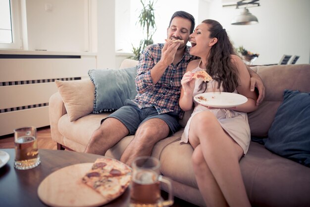 リビング ルームでピザを食べて幸せな若いカップル