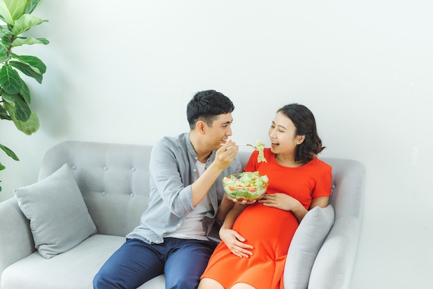 Счастливая молодая пара вместе едят салат на диване в гостиной