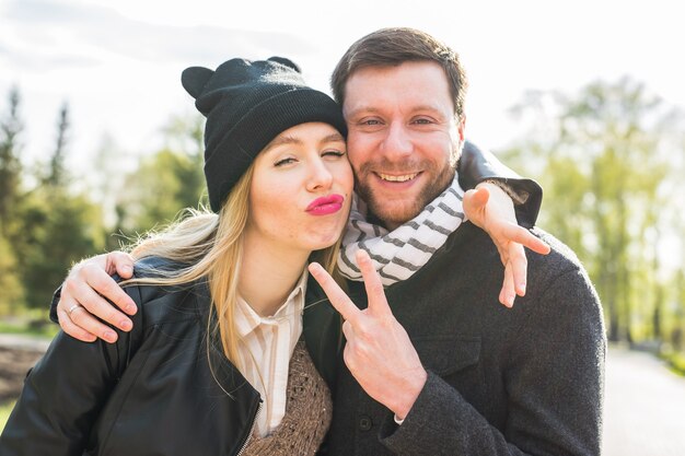 Happy young couple embracing smiling, showing victory sign.