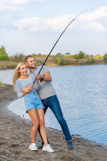 Happy young couple fishing by lakeside