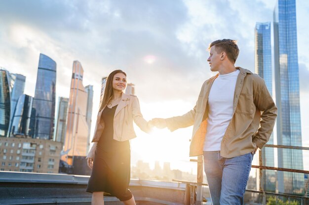 Happy young couple girl man guy on romantic love date on roof top with city skyscraper view panorama Urban summer dating hugging kissing having fun together Boyfriend and girlfriend lovestory