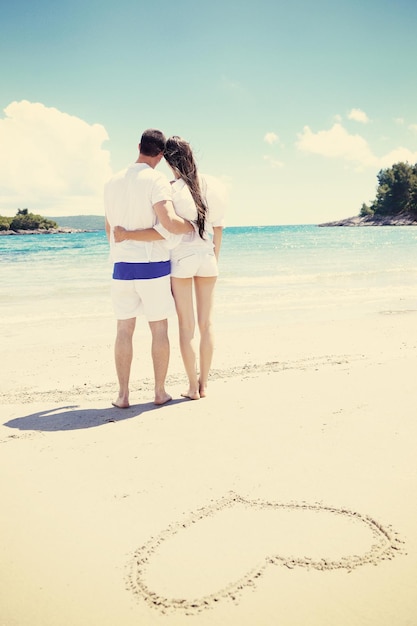 happy young couple have fun and relax  on the summer with heart drawing on beach sand