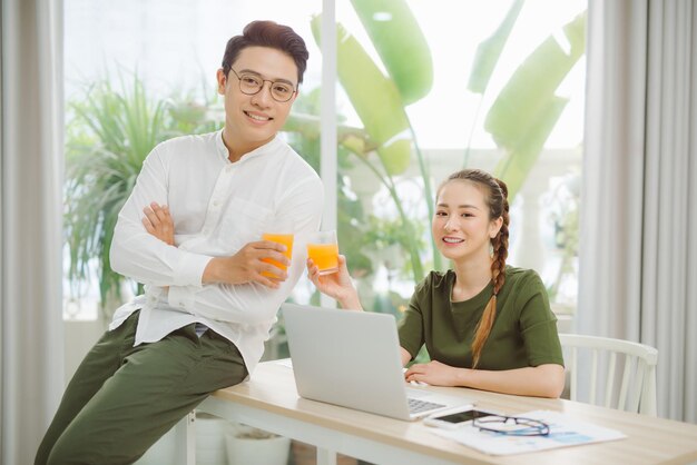 Happy young couple holding glasses of orange juice at the living room and looking to each othe